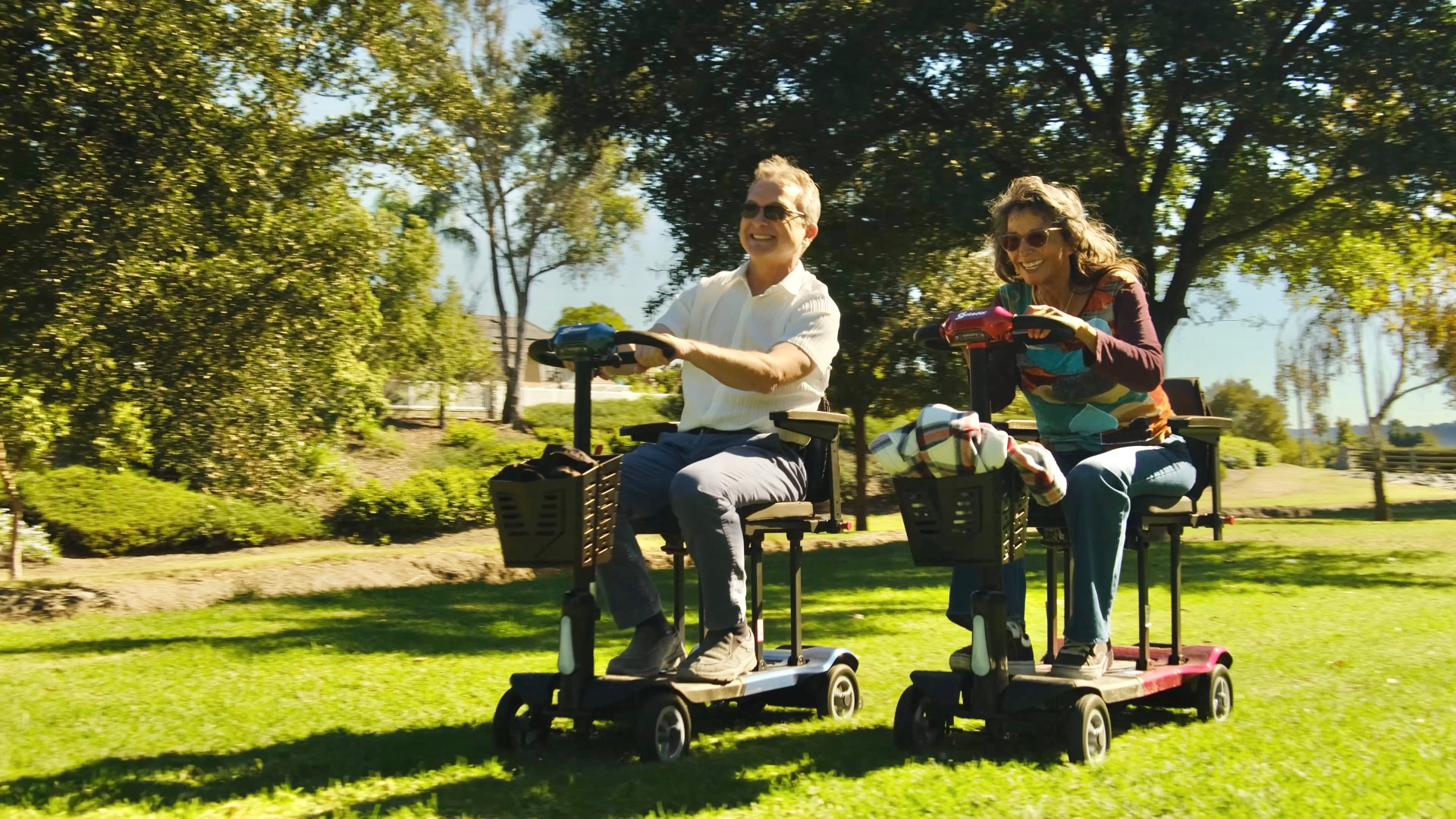 Couple riding mobility scooters across a park